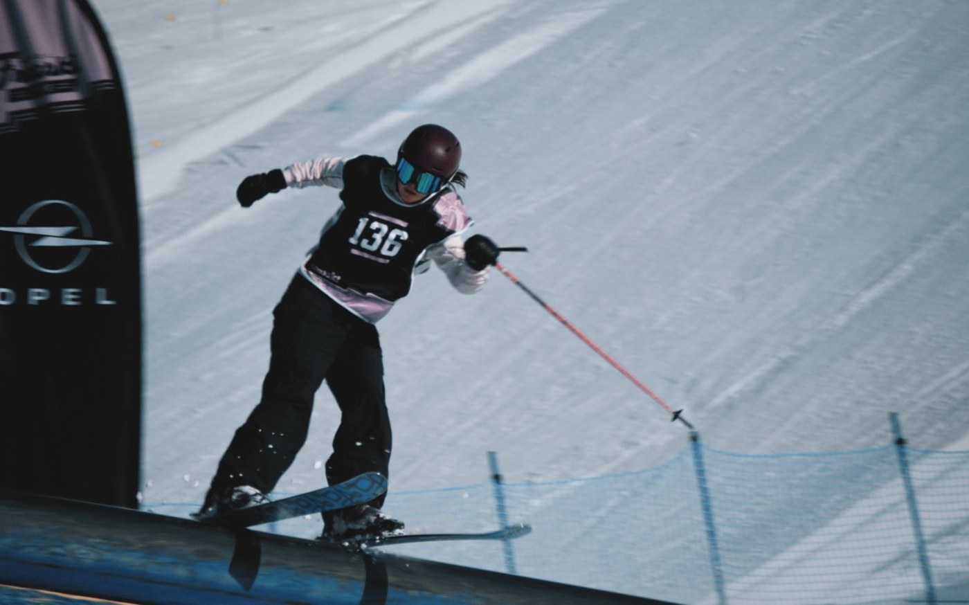 Athletin fährt im Rennanzug durch ein Tor am Davos Open, Opel-Bande im Vordergrund