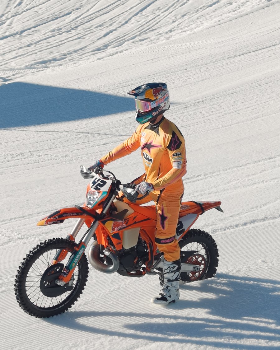 Franjo von Allmen in orangem KTM-Outfit steht neben seiner KTM Motocross-Maschine im Schnee