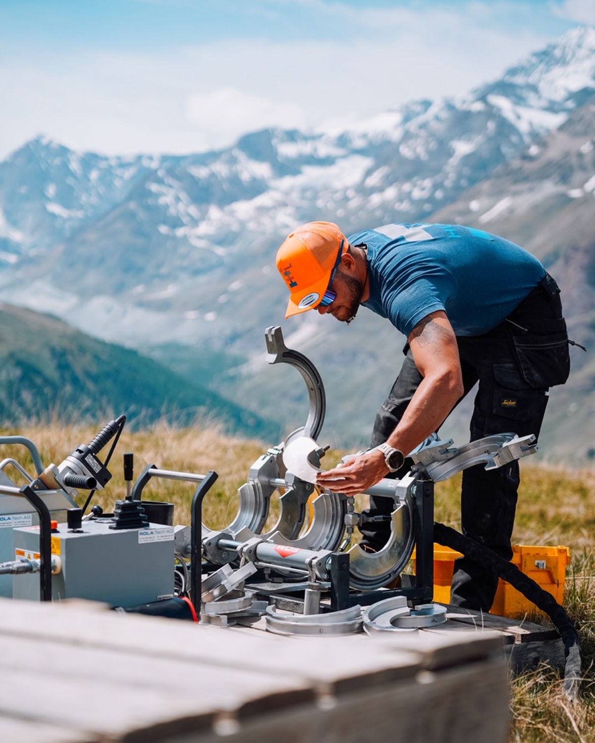 Mitarbeiter der Kilian Huber GmbH bedient eine Rohrschweissmaschine vor Bergpanorama