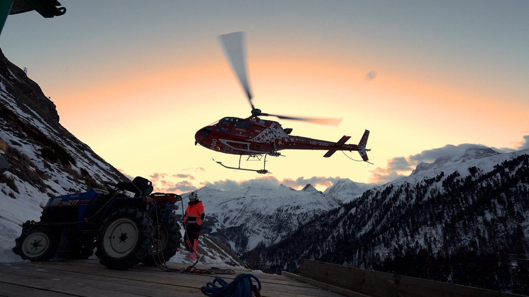 Helikopter fliegt bei Sonnenuntergang zu einer hochalpinen Baustelle an