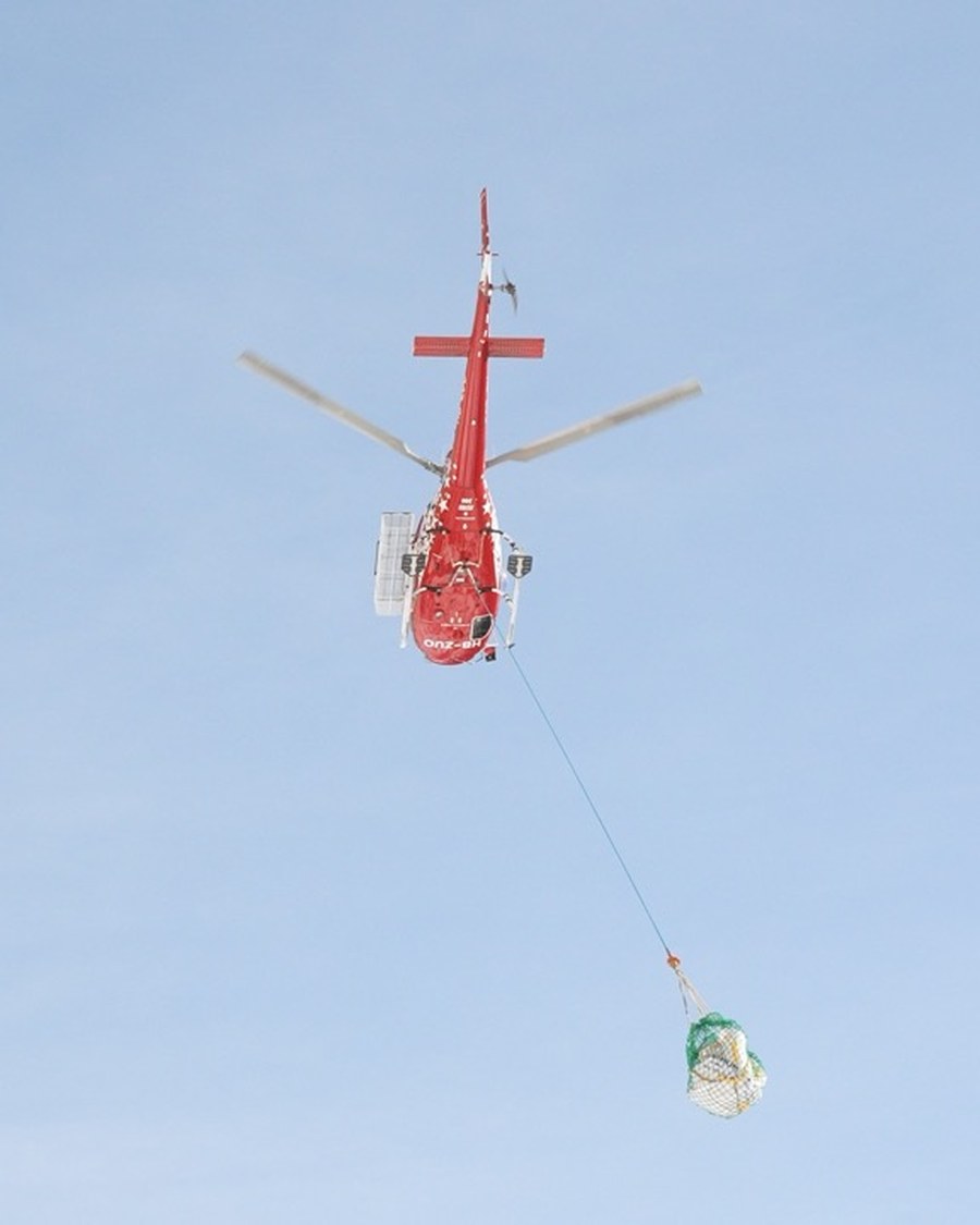 Helikopter transportiert eine Materiallast am Langseil vor blauem Himmel