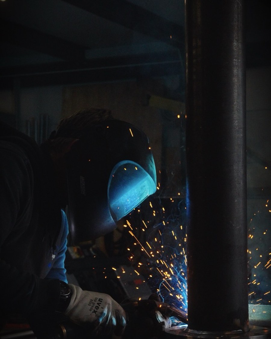 Schweisser bei der Arbeit an einem Stahlrohr in der Werkstatt, Funkenflug