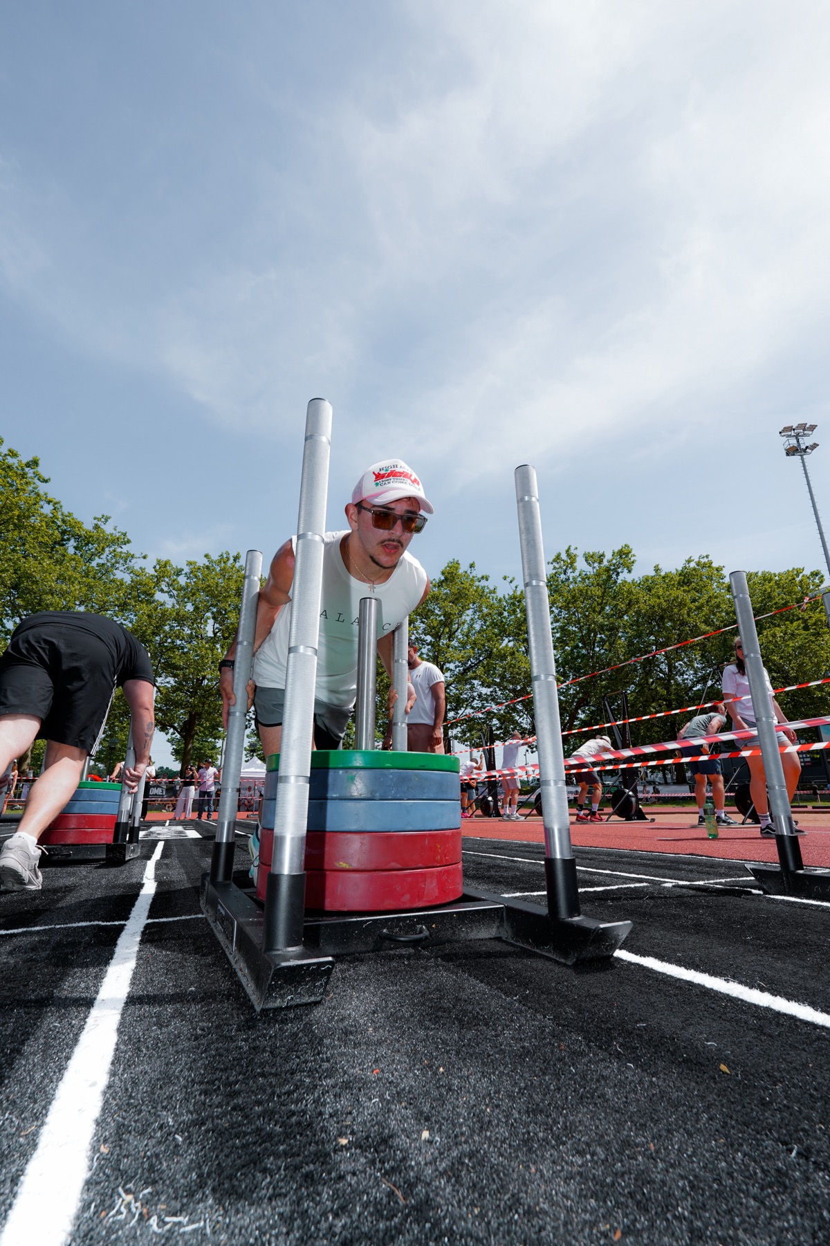 Athlet beim Sled-Push, Zuschauer:innen am Streckenrand