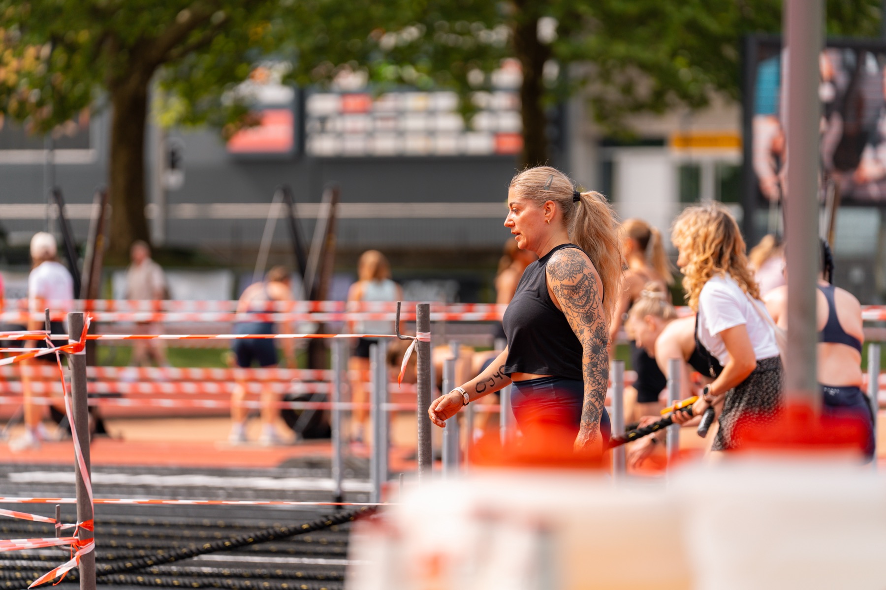 Athletin mit Tattoos geht an der Absperrung entlang, im Hintergrund wird trainiert